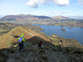 After the climb comes the descent: a hillwalker uses poles as they descend Catbells toward Derwentwater.